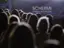 Una folla di persone rivolta verso un cartellone blu con la scritta "SCHERMI CINEMA MULTIPIAZZA", con un'illuminazione soffusa sullo sfondo.