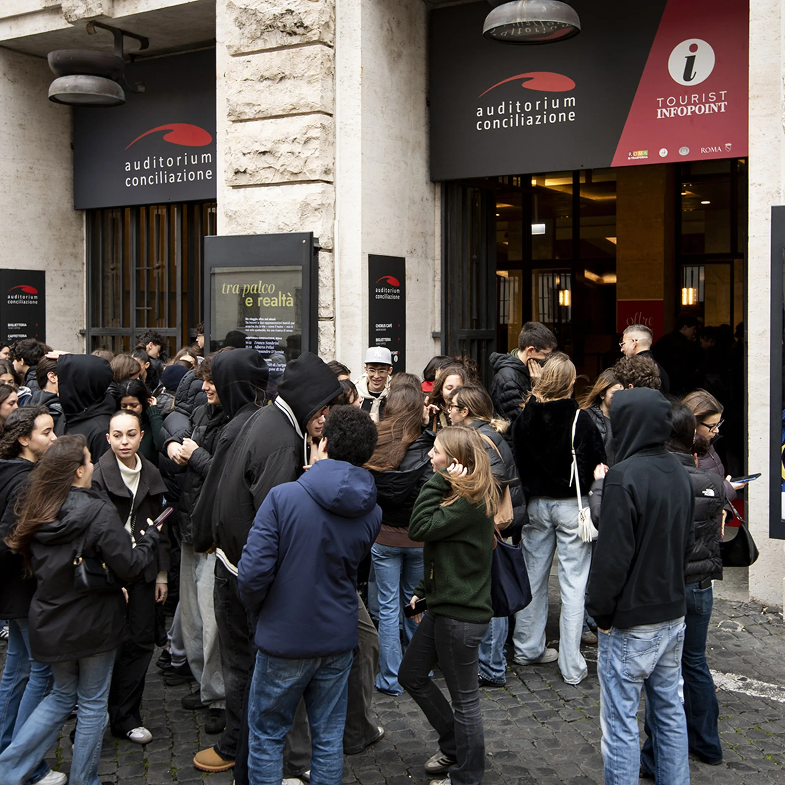 All'ingresso dell'Auditorium Conciliazione, a Roma, si raduna una folla; sono visibili i manifesti dell'evento "Tra Palco e Realtà".