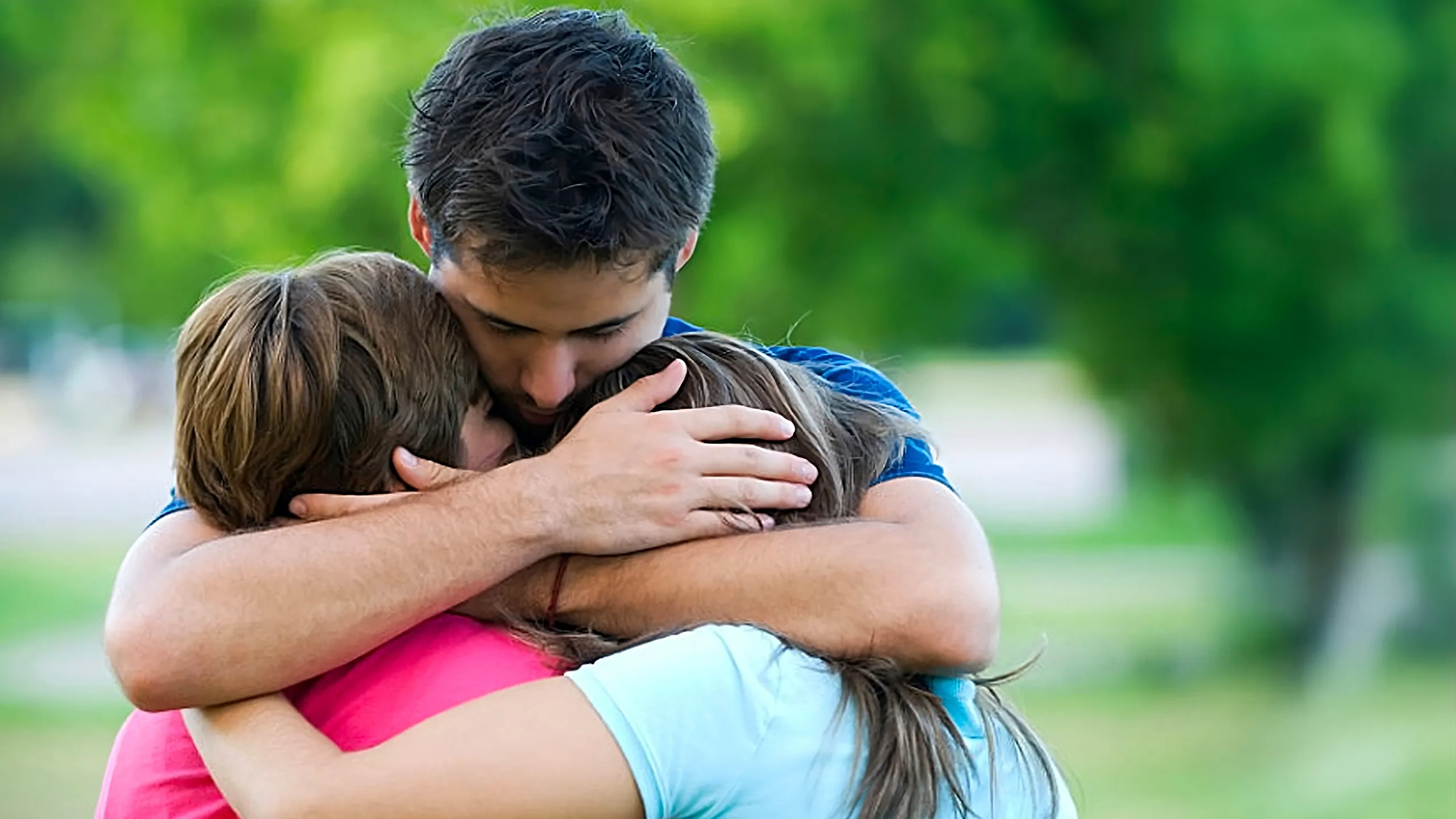 Tre persone si abbracciano all'aperto, circondate dal fogliame verde. Sembrano unite e rassicuranti.