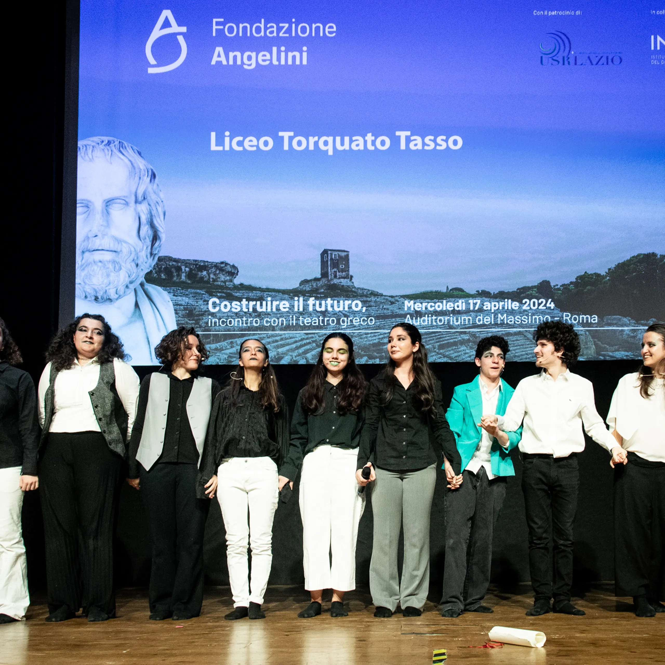 Un gruppo di persone sul palco davanti a uno schermo che mostra i dettagli dell'evento, tra cui “Fondazione Angelini” e “Liceo Torquato Tasso”.