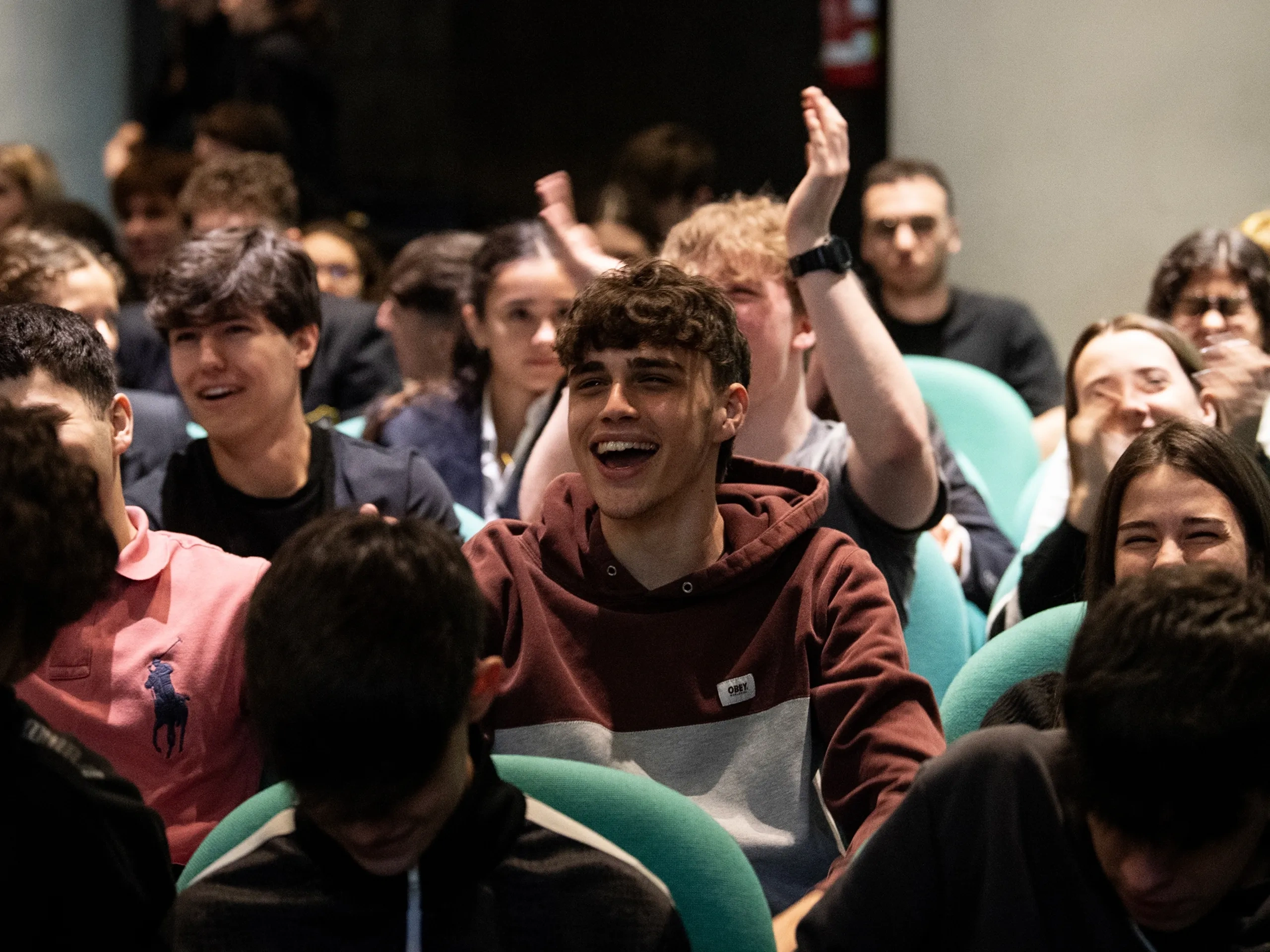 Un folto gruppo di giovani adulti seduti in un auditorium, che ridono e applaudono durante un evento vivace.