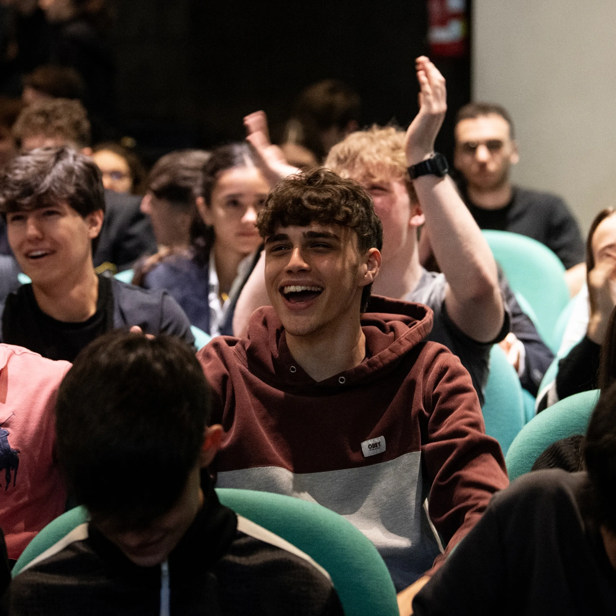 Un folto gruppo di giovani adulti seduti in un auditorium, che ridono e applaudono durante un evento vivace.