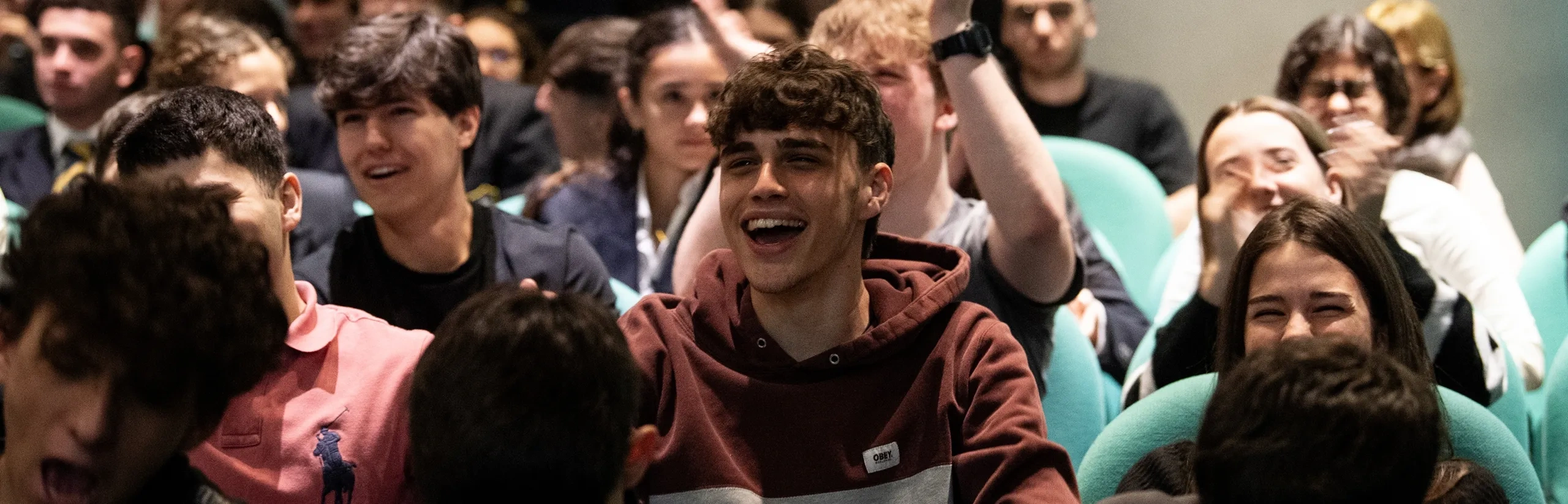 A group of young people sitting in an auditorium, smiling and laughing during an event.