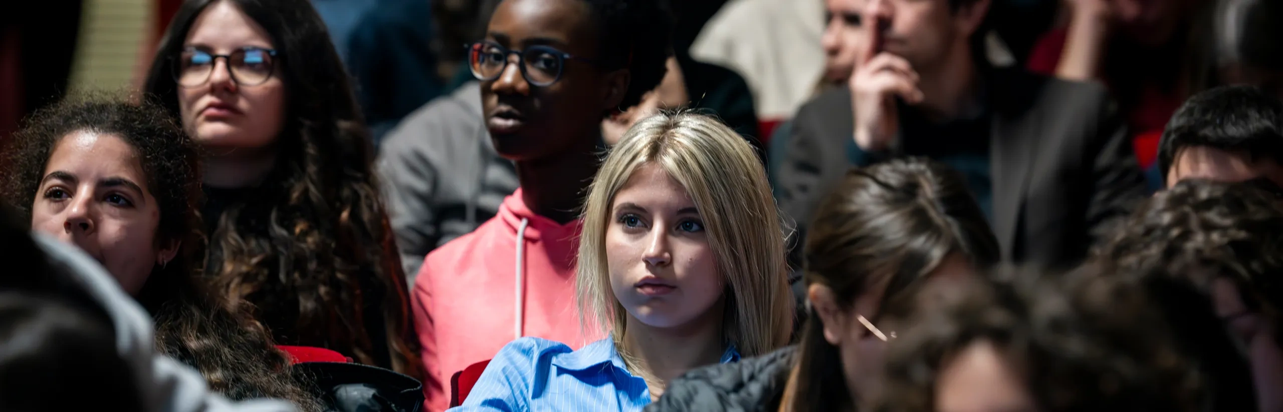 A diverse group of young people sitting in an auditorium, listening attentively to a presentation or event.