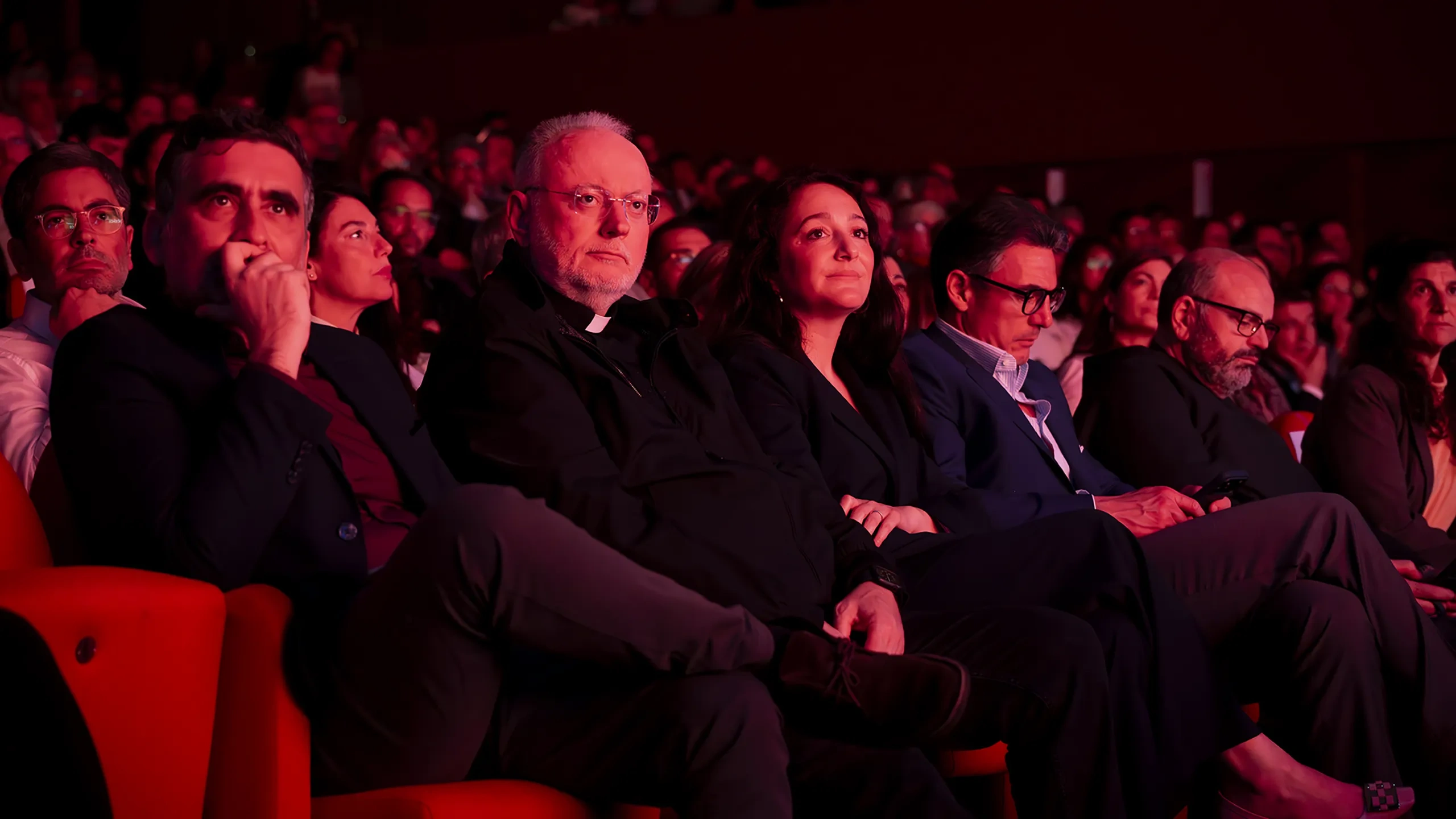 Audience members sitting in a dimly lit theater, attentively watching a performance.
