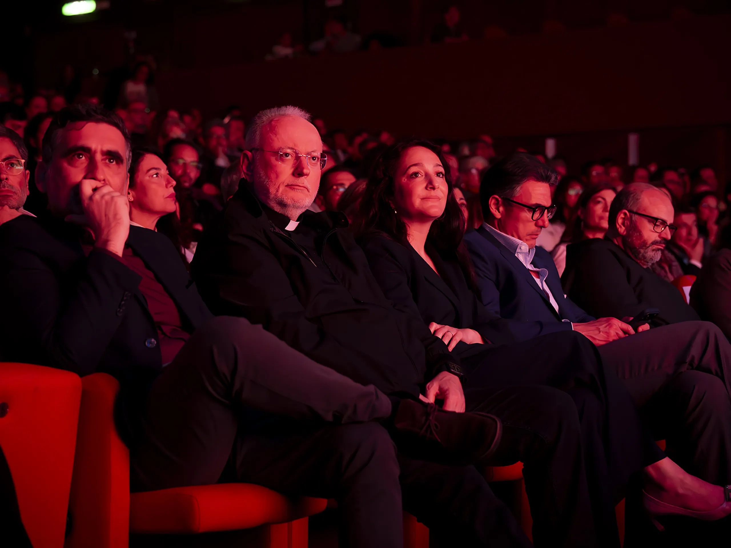 Audience members sitting in a dimly lit theater, attentively watching a performance.