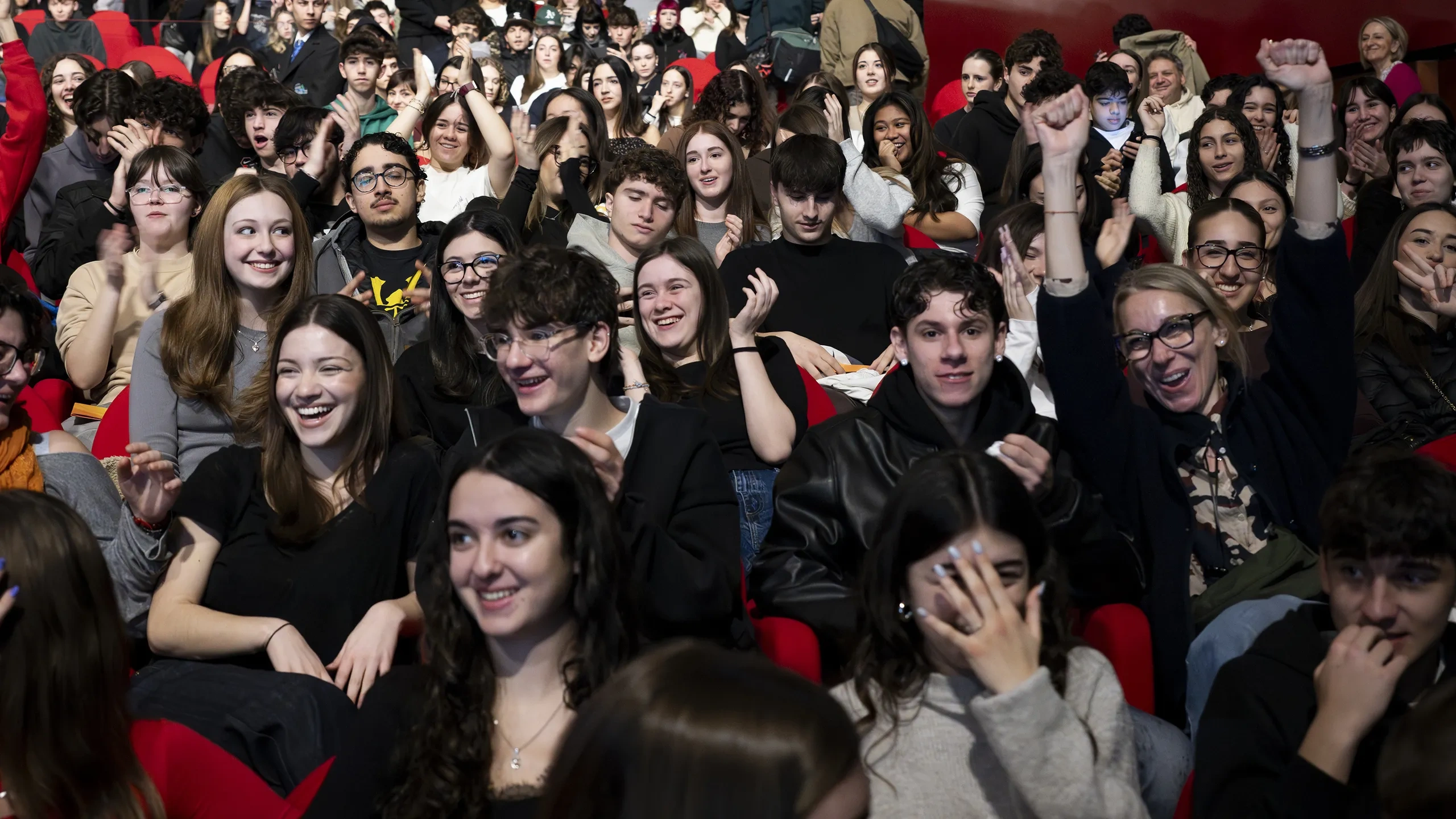 Una grande folla festante seduta in un teatro, con persone che applaudono e sorridono, creando un'atmosfera vivace ed entusiasta.