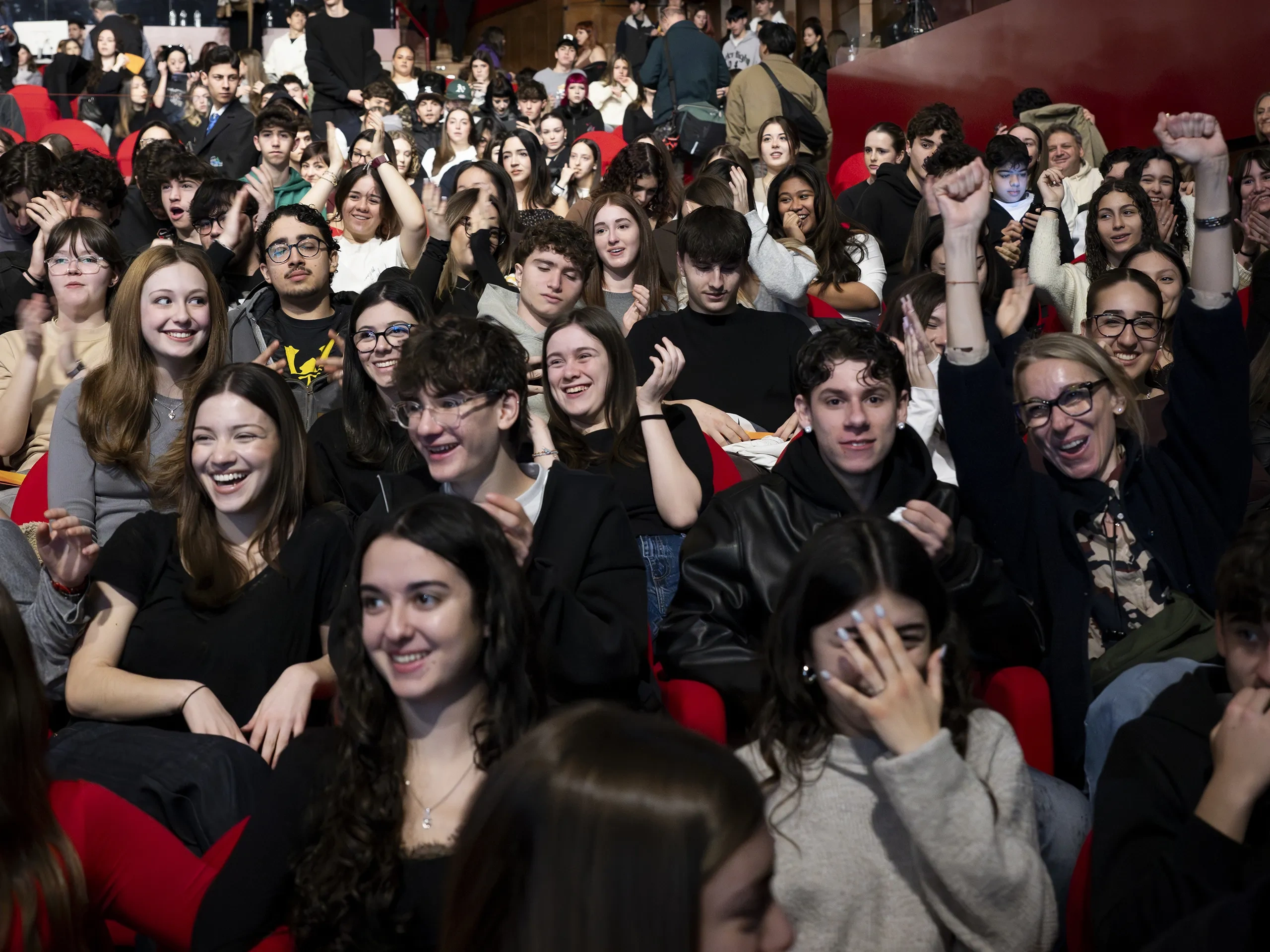 Una grande folla festante seduta in un teatro, con persone che applaudono e sorridono, creando un'atmosfera vivace ed entusiasta.